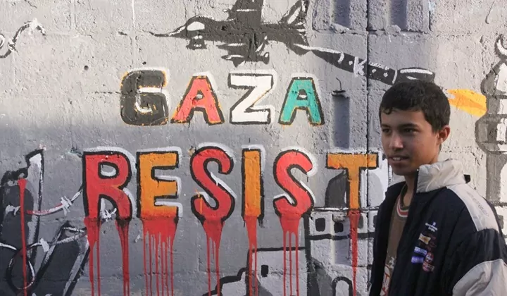 A Palestinian boy stands next to graffiti that reads "Gaza Resist"